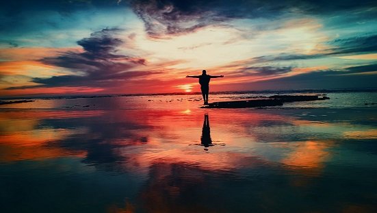 Uma luz suave surgindo atrás de uma pessoa meditando ao nascer do sol, simbolizando clareza espiritual e propósito de vida